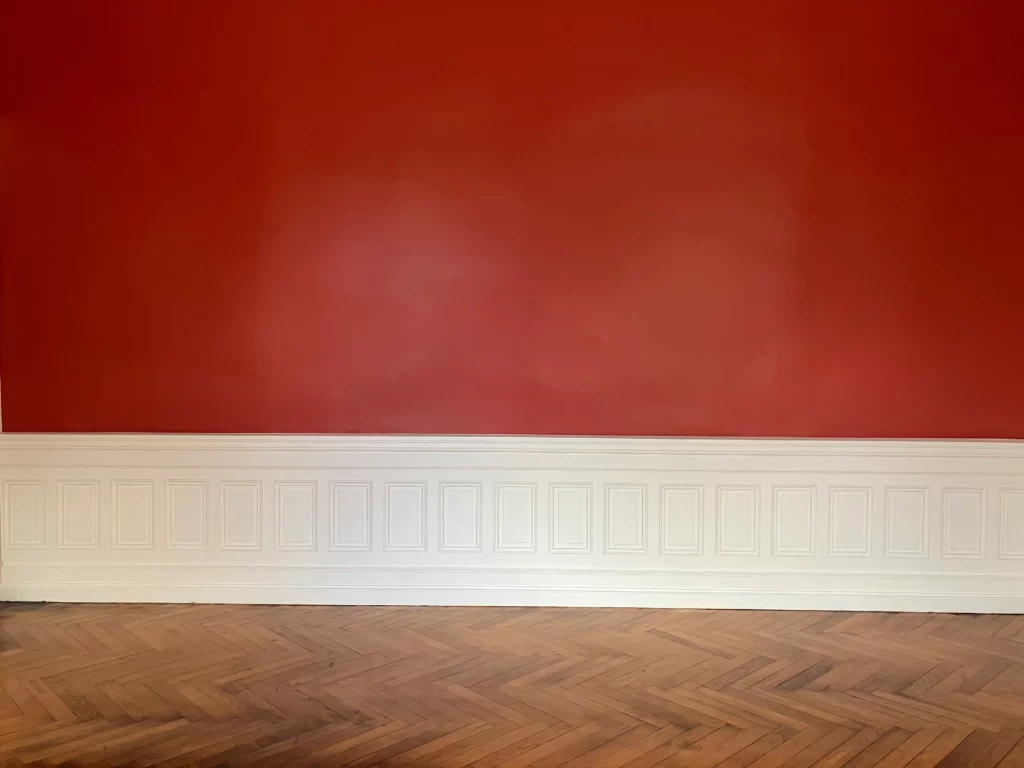 Mur rouge, parquet et moulures verticales du grand salon restauré.