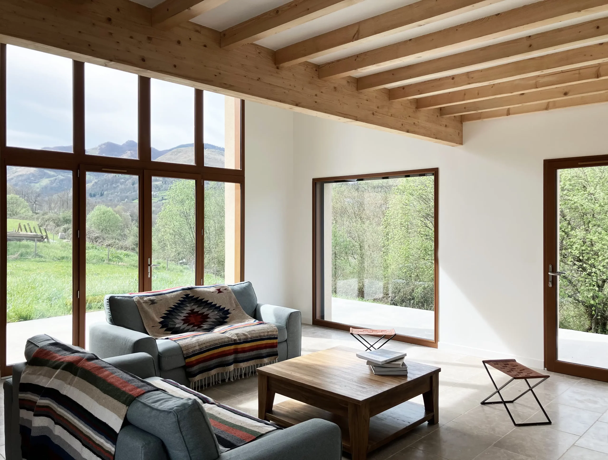 Salon ouvert avec poutres apparentes et grande baie vitrée, maison neuve à Bun.